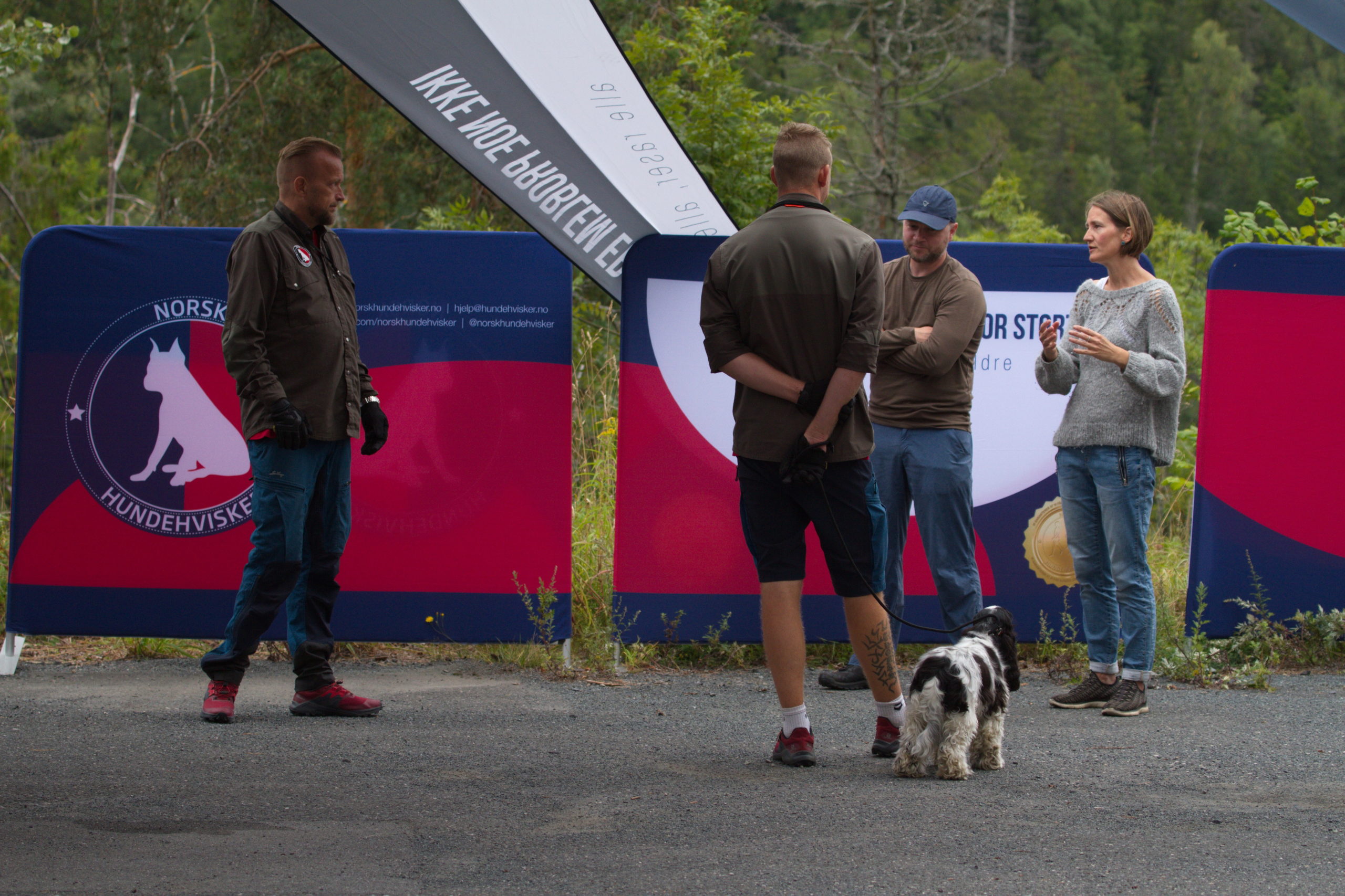 Instruktør og kursdeltakere fra Norsk Hundehvisker i samtale ved informasjonsteltet – hund på bånd i forgrunnen